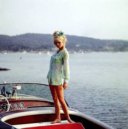 A woman standing on the deck of a classic mahogany motorboat